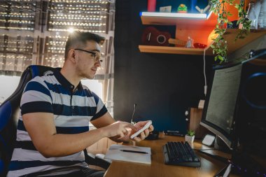 Masada oturan beyaz bir gencin masaüstü bilgisayarının monitörüne bakması kripto döviz kurunu analiz etmesi yatırımını izlemesi veya gerçek insanları satması.