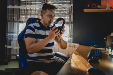 Kafkasyalı genç bir erkek, elinde kulaklıklarla karanlık odada bilgisayarında video oyunları oynuyor. Gerçek insanlar uzay kopyaları yapıyor.