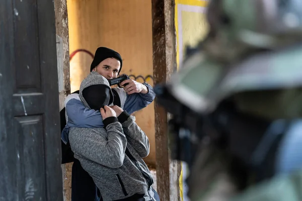 Front view on criminal or terrorist holding unknown hostage pointing gun to his head threatening to kill while unknown soldier or special police force swat is standing in front aiming during rescue