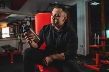 Yetişkin bir adamın ön görüntüsü. Beyaz bir erkek sporcu spor salonunda bankta oturuyor. Elinde koyu siyah bir takviye aleti tutarken vücut geliştirme ağırlık kaldırma ve fotokopi çekmede fren yapıyor.