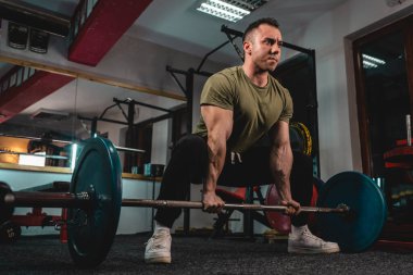 Yetişkin, beyaz, erkek, vücut geliştirme eğitimi almış bir adam spor salonunda dikilirken ağırlık kaldırıyor. Üzerinde koyu renk bir fotoğraf var. Gerçek insanlar uzay manzarası kopyalıyor.
