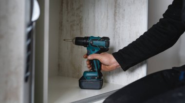 Beyaz tenli bir erkek elektrikli kablosuz tornavida kullanıyor. Evdeki marangozda mobilya montajı yapıyor.