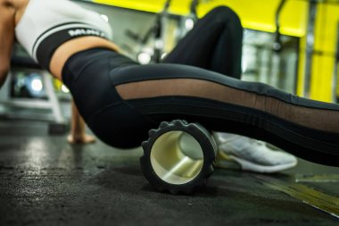 Kas ve Fasya esneme bacağı için siyah köpük paten kullanan kadın sporcu spor salonunda idman yaptıktan sonra ağrılı kasları gevşetiyor - sağlık ve spor vücut bakımı kavramı bacağa yakın