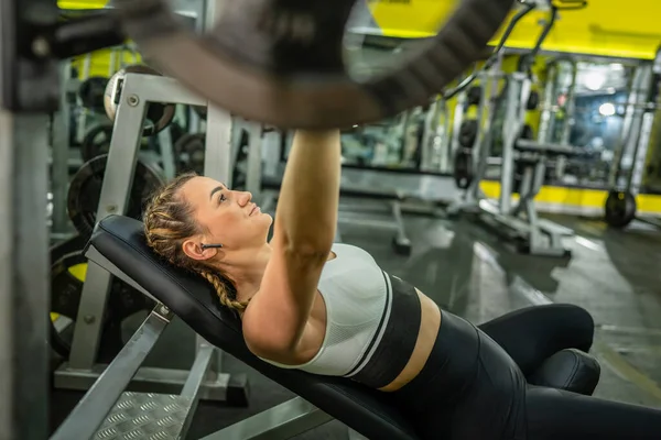 Side view of one caucasian woman female athlete training at gym holding barbel with weights while lying on the bench pushing exercise training chest muscles health and fitness concept copy space