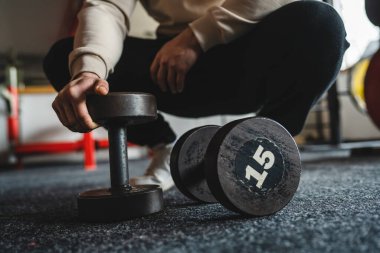 Spor salonunda ve vücut geliştirme konseptinde kimliği belirsiz beyaz adamın el ve dambıllarına yakın durun.