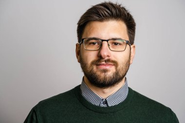 30 yaşında, sakallı, gözlüklü, beyaz arka planda kameraya bakan genç bir beyaz adamın portresi. Süveter giyen genç iş adamı başarısı konsepti.