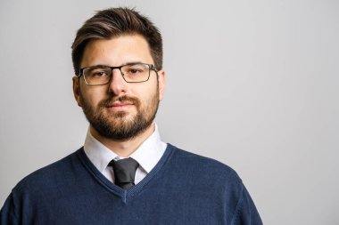 30 yaşında, sakallı, gözlüklü, beyaz arka planda kameraya bakan genç bir beyaz adamın portresi. Süveter giyen genç iş adamı başarısı konsepti.