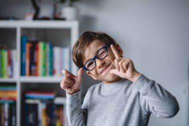 Küçük mutlu, beyaz bir çocuk kameraya yakından bakarken gözlük takıyor, alay ediyor ve gerçek insanlara jest yapıyor. Mutluluk ve neşe dolu çocukluk konseptini kopyalıyor.