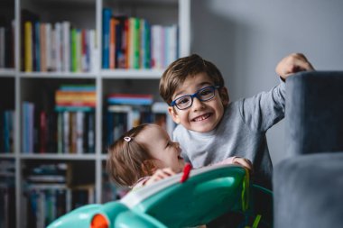 Beş yaşında, gözlüklü mutlu beyaz bir çocuk. Evde kız kardeşiyle oynarken eğleniyor. Gerçek insanlar çocukluk ve aile bağı kurarken eğleniyor.