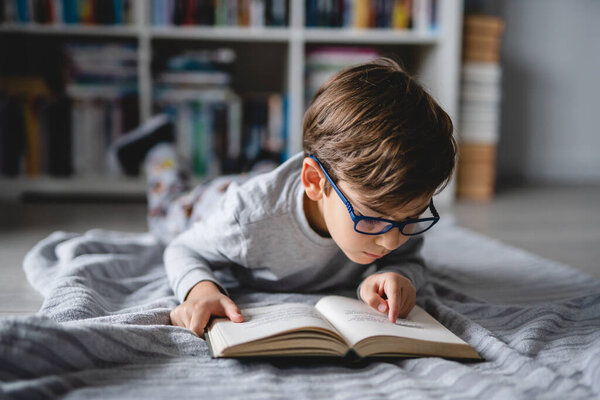Один кавказский мальчик лежал на полу дома в день читая книгу фронтальный вид копировать пространство реальных людей образовательная концепция