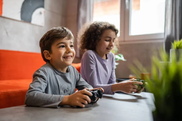 两个孩子小高加索兄弟姐妹快乐的孩子兄弟姐妹男孩和女孩坐在家里玩电玩控制台的时候用控制杆或控制器真人家庭休闲的概念 — 图库照片