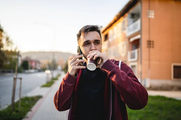 秋の夜に街を歩いている大人の若い白人男性の正面図携帯電話とコーヒーのカップを使用して半分の長さの本物の人々は側に見えるスペースをコピーします — ストック写真