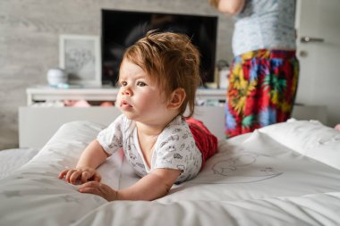 Beyaz bebek, evinde, aydınlık odada, göbeğinin üstünde yatarken annesi de arkasında dikilip gerçek insanların çocukluk ve aile kavramlarını değiştirecek kıyafetler arıyor.