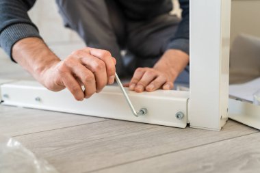 Kimliği belirsiz beyaz bir erkek evde yerde oturuyor. Eşyaları birleştiriyor. Elinde parçaları ve talimatları tutuyor.