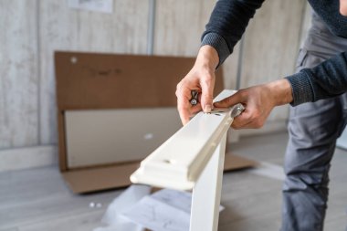 Kimliği belirsiz beyaz bir erkek evde yerde oturuyor. Eşyaları birleştiriyor. Elinde parçalar ve talimatlar tutuyor.