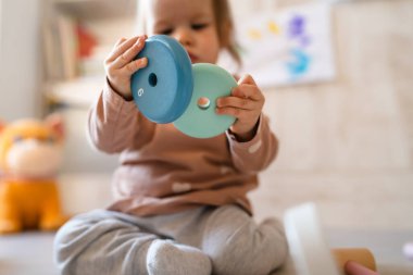 Küçük beyaz bir kız bebek fotokopi odasının zemininde oynuyor. Elinde gündüz gözüyle tahta oyuncaklar var.