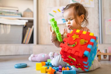Küçük, beyaz bir kız. Evdeki fotokopi odasında yerde oynuyor. Elinde plastik oyuncaklar var.