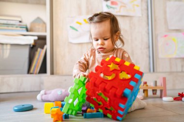 Küçük, beyaz bir kız. Evdeki fotokopi odasında yerde oynuyor. Elinde plastik oyuncaklar var.
