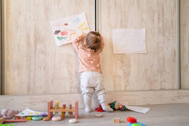 Küçük bir kız bebek bakışı, ayakta duran bir bebek kadar uzun. Evdeki duvara resim çiziyor. Gerçek insanlar uzay ailesinin çocukluk gelişimini ve büyüme kavramını kopyalıyor.