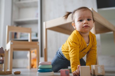 Küçük beyaz bir kız bebek fotokopi odasının zemininde oynuyor. Elinde gündüz gözüyle tahta oyuncaklar var.