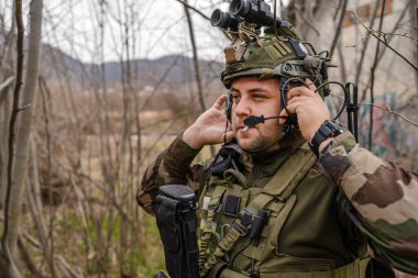 Kamuflaj üniformalı bir askerin cephedeki portresi. Silahlı ve savaş alanına gitmeye hazır. Doğada duruyor, paralı askerlerin kamera köpeklerine bakıyor ya da gönüllü.