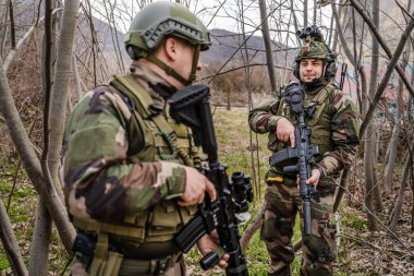 Kamuflaj üniformalı askerlerin cephedeki portresi. Silahlı ve savaş alanına gitmeye hazır. Doğada durup paralı askerlerin ya da gönüllülerin kamera köpeklerine bakıyor.