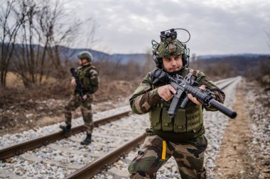 Savaş köpeklerinden iki asker paralı asker üniformalı silahlı adamlar savaş alanında çatışma bölgesinde demiryolunu emniyete alırken görev sırasında devriye bölgesini gözlüyor.