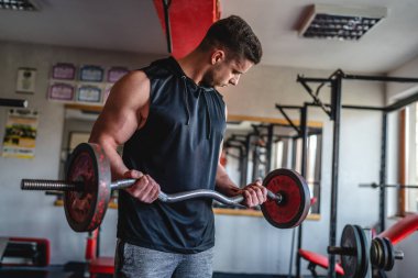 Spor salonunda duran bir genç adam halter ve ağırlık kaslarıyla egzersiz yapıyor erkek vücut geliştirici eğlence amaçlı amatör kaldırıyor gerçek insanları taklit ediyor.