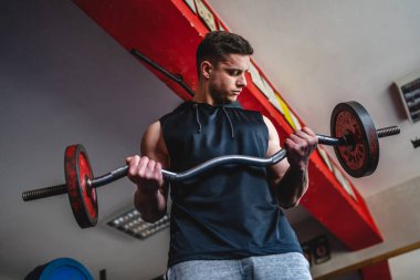 Spor salonunda duran bir genç adam halter ve ağırlık kaslarıyla egzersiz yapıyor erkek vücut geliştirici eğlence amaçlı amatör kaldırıyor gerçek insanları taklit ediyor.