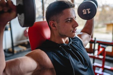 Yetişkin bir erkek, beyaz erkek, omuz geliştiriyor. Salonda otururken halterli kaslara baskı yapıyor. Gerçek insanlar uzay kopyaları yapıyor.