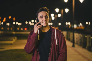 Genç, beyaz bir adamın portresi. Şehir ya da kasabada gece vakti elinde cep telefonuyla dikiliyor. Fotokopi çekerek konuşuyor.