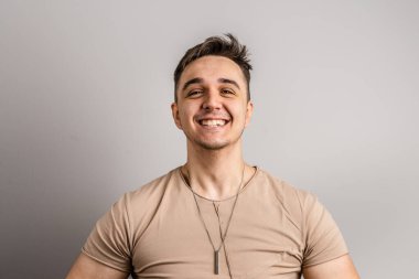 Yetişkin beyaz bir adamın portresi. 25 yaşında. Arka planda beyaz bir duvarın önünde kameraya bakıyor.