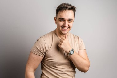 Yetişkin beyaz bir adamın portresi. 25 yaşında. Arka planda beyaz bir duvarın önünde kameraya bakıyor.