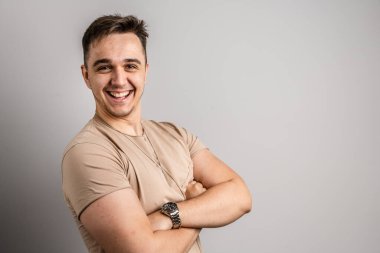 Yetişkin beyaz bir adamın portresi. 25 yaşında. Arka planda beyaz bir duvarın önünde kameraya bakıyor.