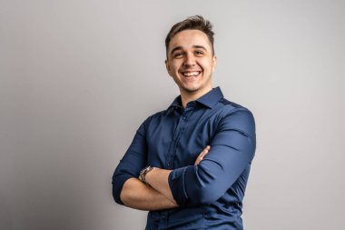 Yetişkin beyaz bir adamın portresi. 25 yaşında, beyaz duvarın önünde kameraya bakıyor. Arka planda gülümsüyor, günlük mavi gömlek fotokopi alanı giyiyor.