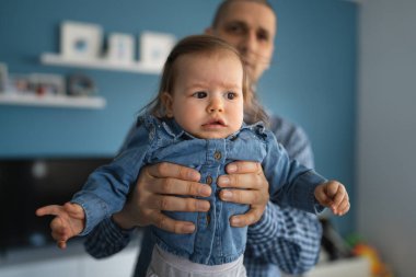 İki kişi, küçük beyaz bir kız, babasının elinde. Yetişkin bir adam, kızını kucağında tutuyor. Mavi gömlekli, gerçek bir aile babası ve büyüyen bir konsept.