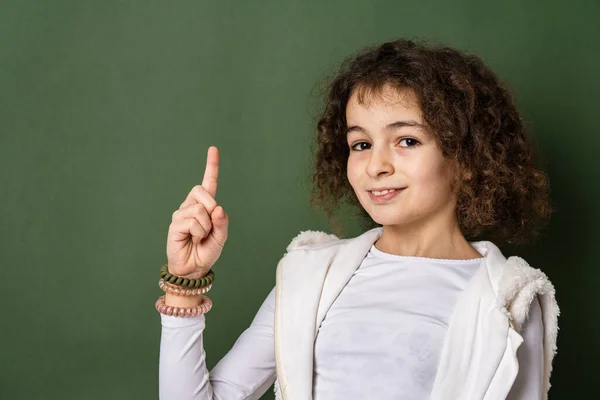 一位10岁的高加索小女孩 卷曲的前景肖像画站在绿色背景前 看着摄像机的手指 笑着笑着模仿太空 — 图库照片