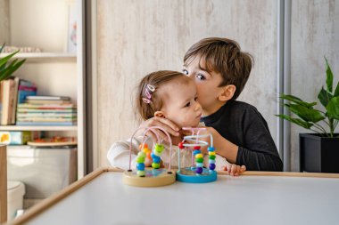 Küçük beyaz bir oğlan, beş yaşında. Küçük kız kardeşini öpüyor. Evde, aydınlık bir odada oyun oynarken.