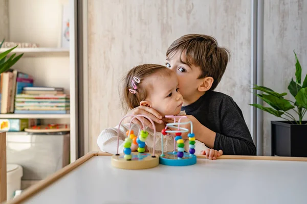 Küçük beyaz bir oğlan, beş yaşında. Küçük kız kardeşini öpüyor. Evde, aydınlık bir odada oyun oynarken.
