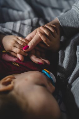 Bebek annesinin elini tutarken, elinde annesinin baş parmağını tutan küçük bir kız çocuğu vardı. Gecenin karanlığında uyuyordu. Çocukluk bakımı ve annelik kavramı.