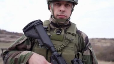 Kamuflaj üniformalı bir askerin cephedeki portresi. Silahlı ve savaş alanına gitmeye hazır. Doğada duruyor, paralı askerlerin kamera köpeklerine bakıyor ya da gönüllü.