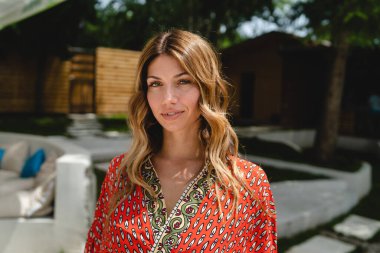 Güneşli bir yaz gününde, açık havada duran, kırmızı elbiseli güzel bir esmer kadının portresi. Kameraya bakıyor. Kendine güvenen mutlu fotokopi alanı.