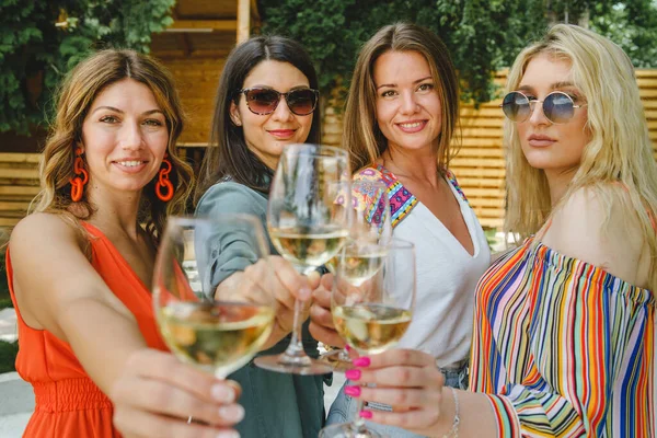 Dört yetişkin güzel beyaz kadın arkadaş ellerinde beyaz şarapla arka bahçede mahsur kalmış yaz tatilinde eğleniyor ve içiyor - gerçek insanlar boş vakitlerinde
