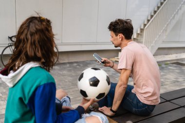 Birkaç kadın ve genç beyaz adam modern mutlu yetişkin erkek ve kadın sevgili gülüşü stadyumun önünde oturmuş futbol topu tutuyorlar ve futbol konsepti fotokopi alanı.