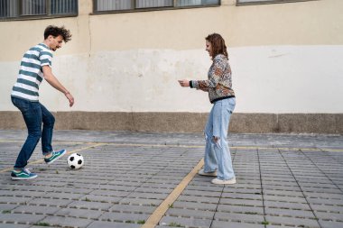 Yandan bakan erkek ve kadın futbol oynayan çift, şehir veya kasabada fotokopi alanının önündeki kaldırımda topa vuran çift.