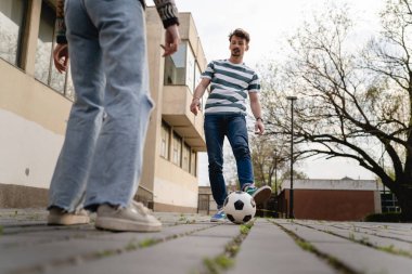 Yandan bakan erkek ve kadın futbol oynayan çift, şehir veya kasabada fotokopi alanının önündeki kaldırımda topa vuran çift.