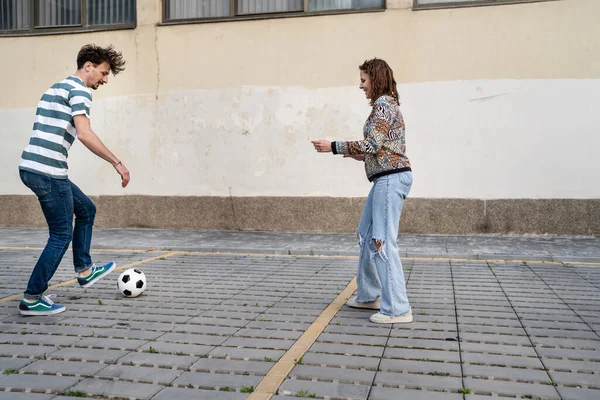Yandan bakan erkek ve kadın futbol oynayan çift, şehir veya kasabada fotokopi alanının önündeki kaldırımda topa vuran çift.