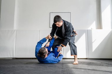 İki Brezilyalı jiu jitsu BJJ sporcusu akademi dövüş sanatları sahasında antrenman yapıyor kimono gi spor üniforması giyiyorlar spor minderlerinde spor jiujitsu ve kendini savunma konsepti fotokopi uzayı