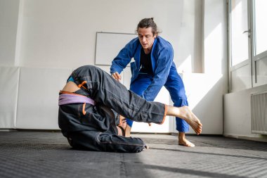 İki Brezilyalı jiu jitsu BJJ sporcusu akademi dövüş sanatları sahasında antrenman yapıyor kimono gi spor üniforması giyiyorlar spor minderlerinde spor jiujitsu ve kendini savunma konsepti fotokopi uzayı