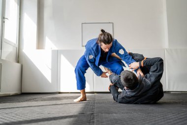 İki Brezilyalı jiu jitsu BJJ sporcusu akademi dövüş sanatları sahasında antrenman yapıyor kimono gi spor üniforması giyiyorlar spor minderlerinde spor jiujitsu ve kendini savunma konsepti fotokopi uzayı
